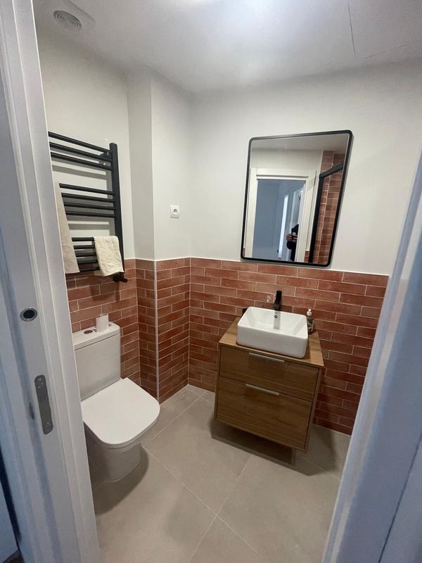 Baño con mueble de madera, lavabo sobre encimera y toallero negro